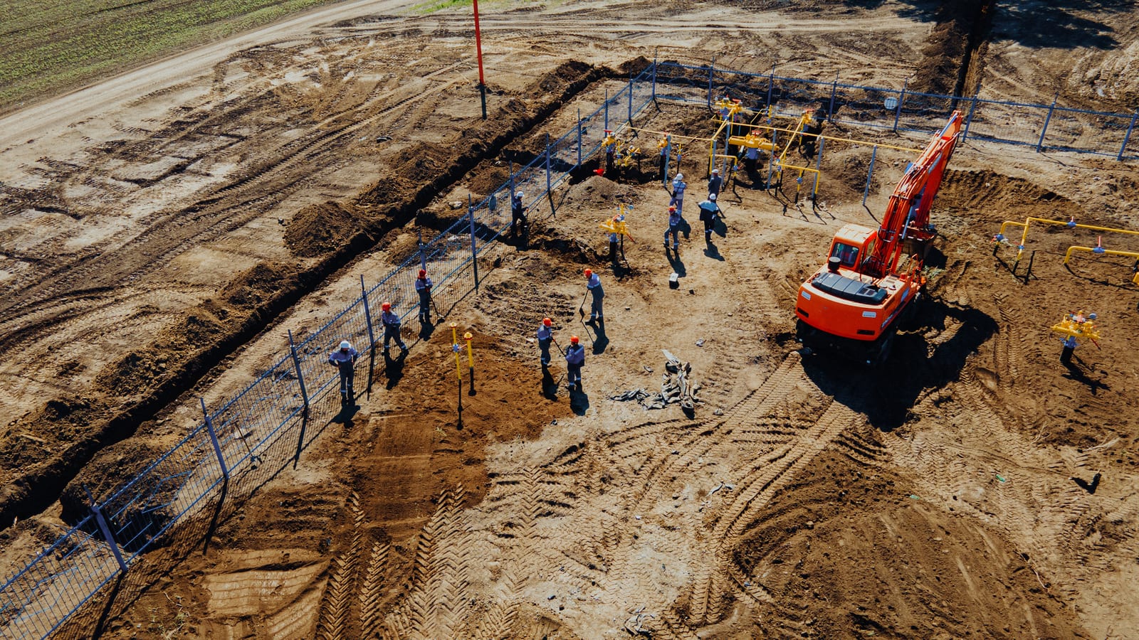 Aerial view of construction workers and an excavator beside a pipe trench